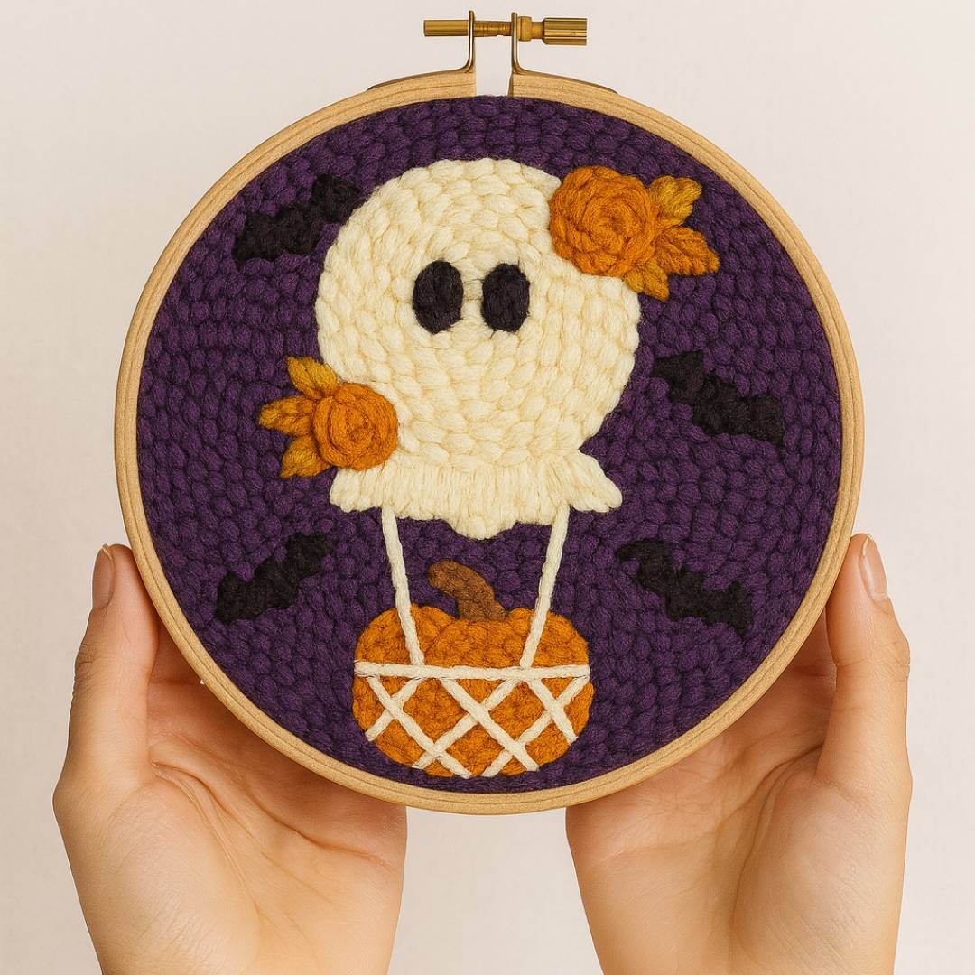 Embroidery hoop with a Halloween-themed ghost design held by hands against a beige background
